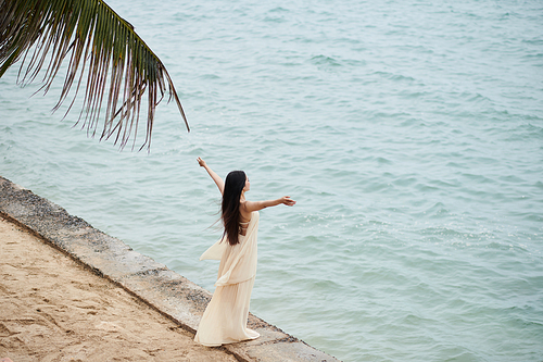 Young woman in long silk dress enjoying sea breeze