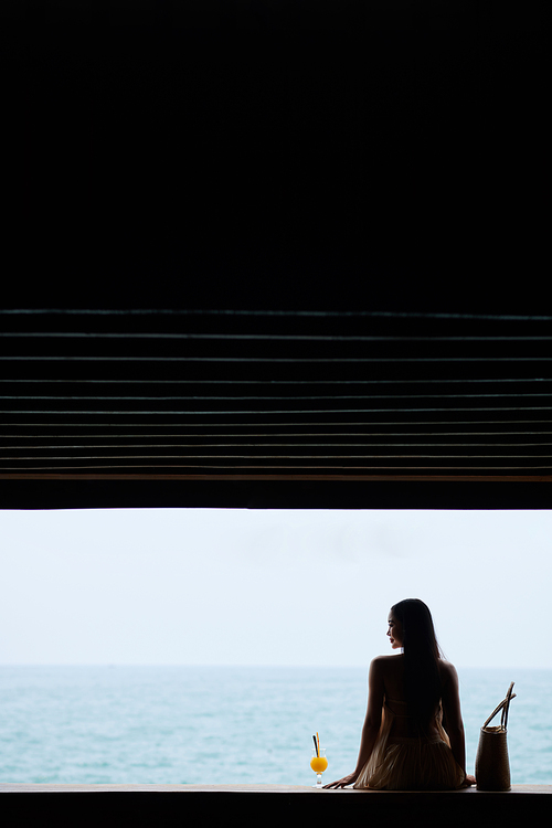 Header with smiling woman in flowing dress sitting next to glass of cocktail and enjoying beautiful seascape