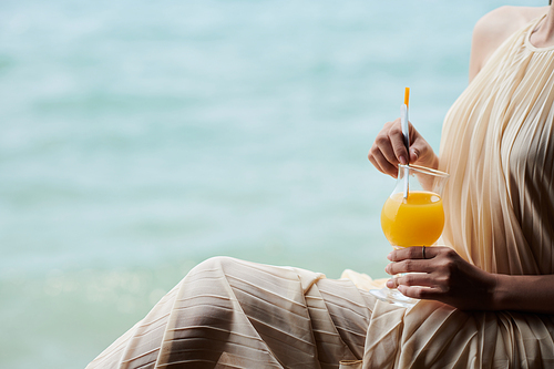 Cropped image of young woman in silk dress drinking orange juice