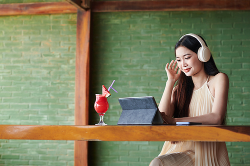 Smiling young woman wearing headphones when video calling coworker or friend