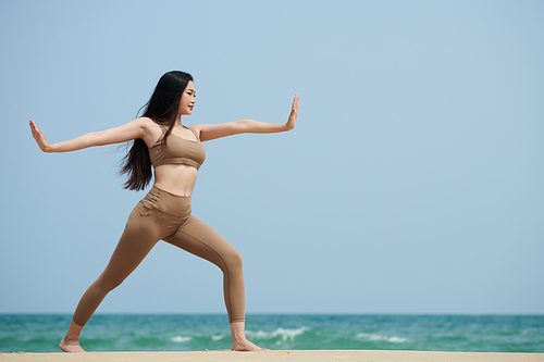 Young woman practicing yoga on sandy beach in the morning