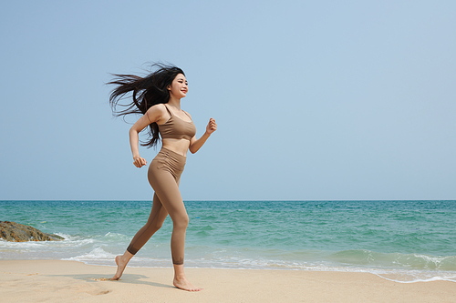 Young Asian woman with long hair jogging on beach in the morning