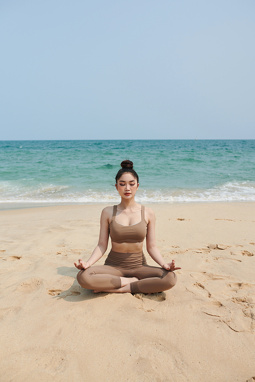 Young woman meditating on beach in the morning
