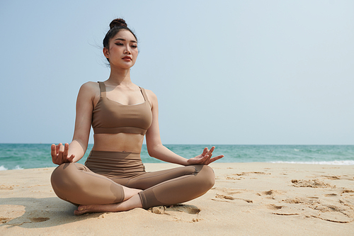 Young Asian woman meditating in lotus position on sunny beach