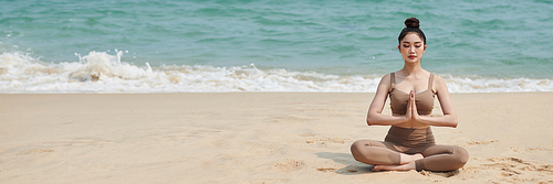Header with young woman meditating in lotus position on sandy beach