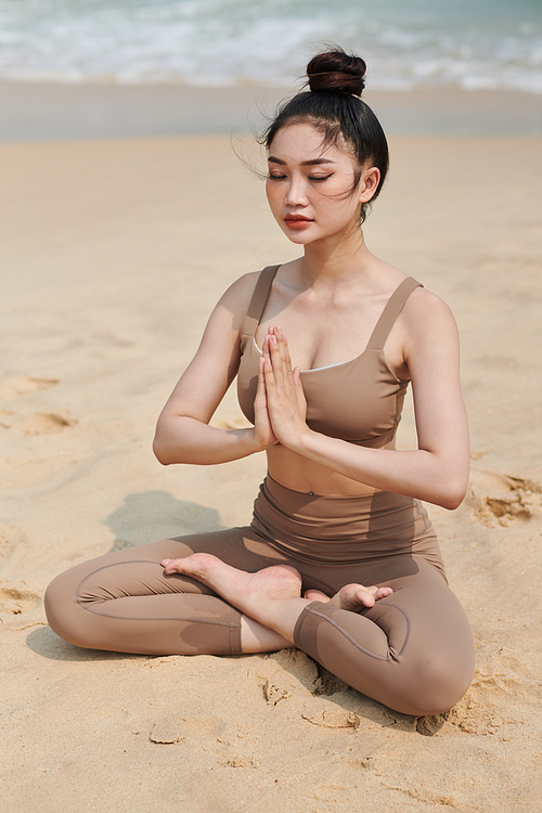 Young woman holding hands in namaste mudra when meditating on beach