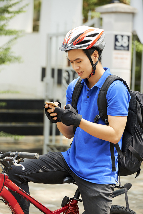 Vietnamese young man sitting on bicycle and setting destination point in navigation app
