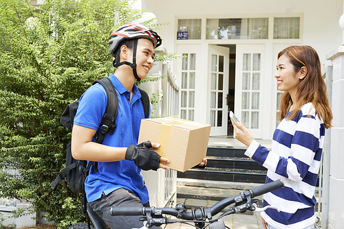 Happy young Asian woman receiving package from delivery man sitting on bicycle