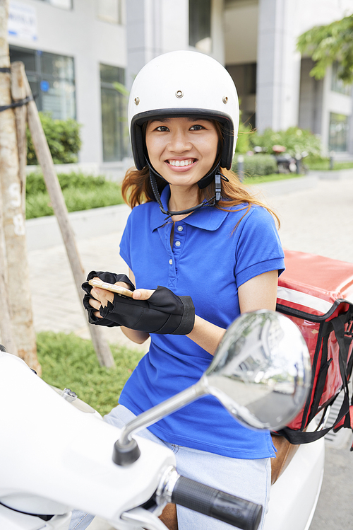 Pretty smiling young Vietnamese woman checking next address on smartphone screen where to deliver food