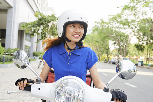 Smiling young Asian delivery woman riding scooter and hurrying to deliver hot food to customers