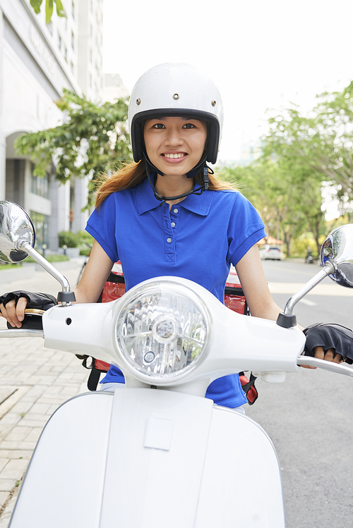 Portrait of lovely young Asian delivery woman in helmet riding scooter to another address