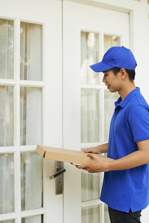 Delivery man in blue uniform bringing package to entrance doors of customer