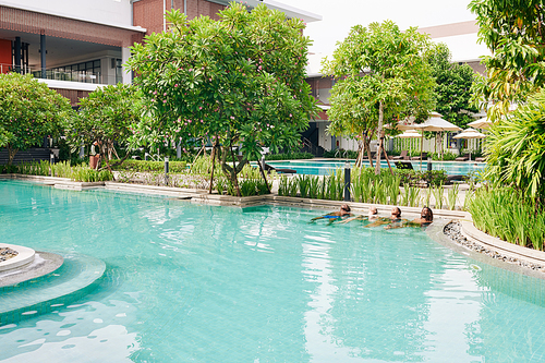 Friends relaxing in swimming pool of spa hotel on sunny summer day, vacation and getaway concept