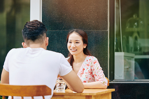 Smiling pretty young Vietnamese woman dating with boyfriend at cafe table