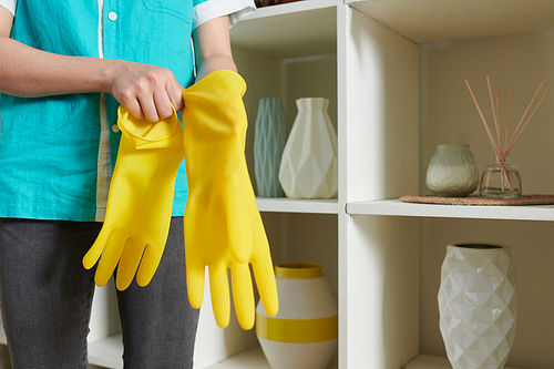 Close-up of cleaner girl putting on yellow rubber gloves before cleaning the room