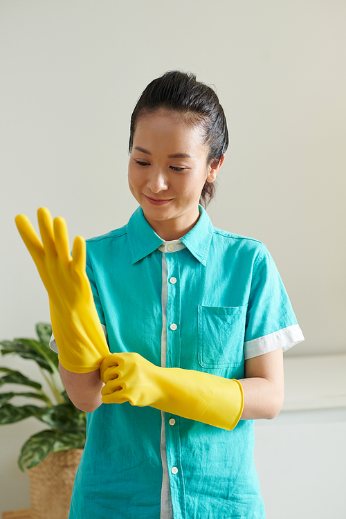 Asian young cleaner putting on uniform and rubber gloves ready to work