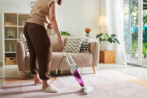 Close-up of housewife using vacuum cleaner to vacuum the carpet in living room during housework at home