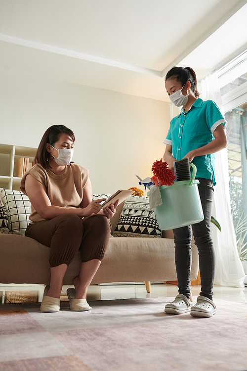 Woman in protective mask using digital tablet to leave feedback of cleaning service worker after her work