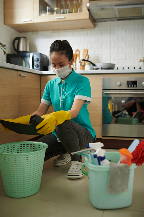 Asian cleaning worker in mask doing housework in domestic kitchen during her work