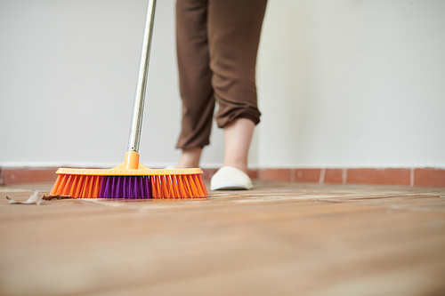 Close-up of woman sweeping wooden floor with mop near her house outdoors