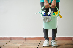 Close-up of cleaning worker holding bucket with different supplies for housework