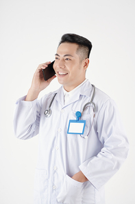 Portrait of positive doctor in white labcoat putting hand in pocket and talking on phone with patient