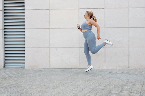 Fit plus size young woman in grey sportswear jogging outdoors in the morning