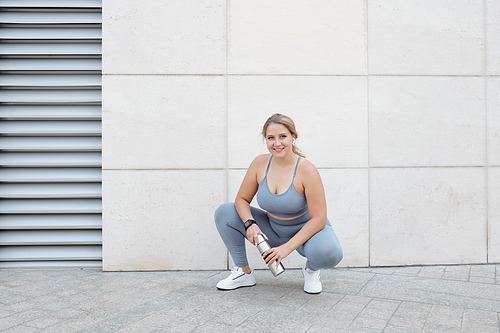 Happy pretty young fit plus size young woman resting after training and drinking water