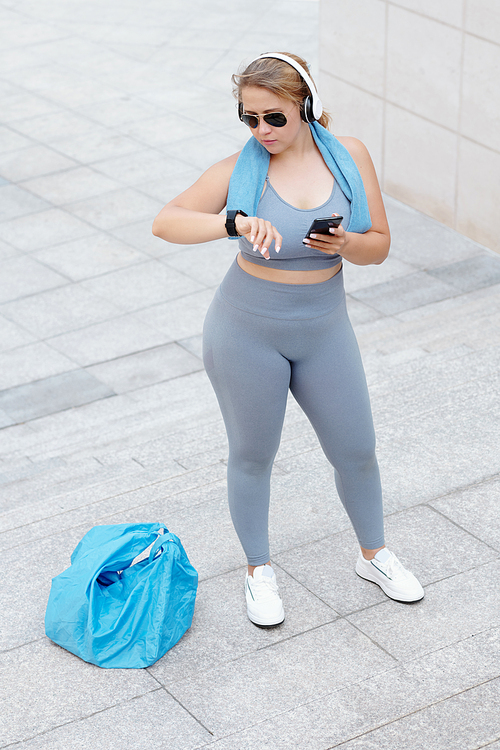 Fit plus size sportswoman in sunglasses and headphones checking health application on her smartwatch