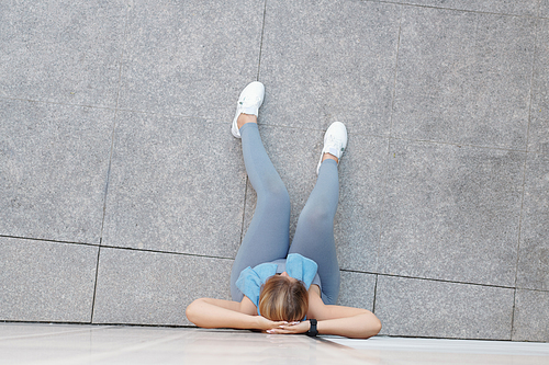 Plus size young woman resting on ground and leaning on wall when resting after intense outdoor training