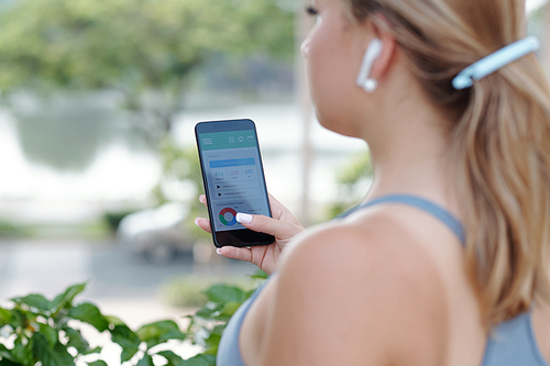 Young woman using application on smartphone when controlling her weight and consumed and burned calories