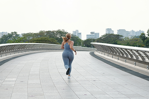 Plus size young woman jogging on empty bridge early in the morning, view from the back, determination concept