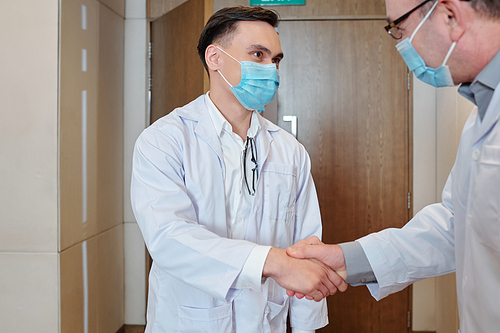 Young scientist in medical mask shaking hand of prominent researcher who invented new vaccine