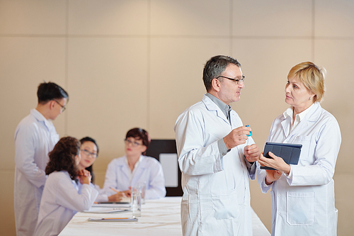 Mature researchers with digital tablet discussing advantages of new vaccine at meeting