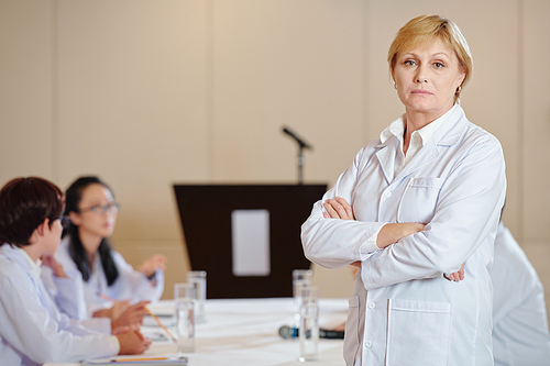 Portrait of serious female researcher in labcoat folding arms and looking at camera