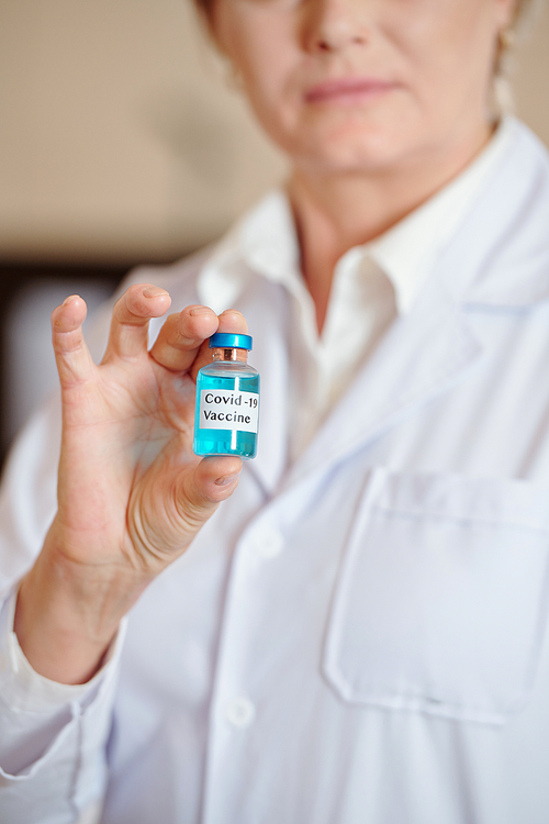 Close-up image of mature female scientist showing vial with new covid-19 vaccine her company created