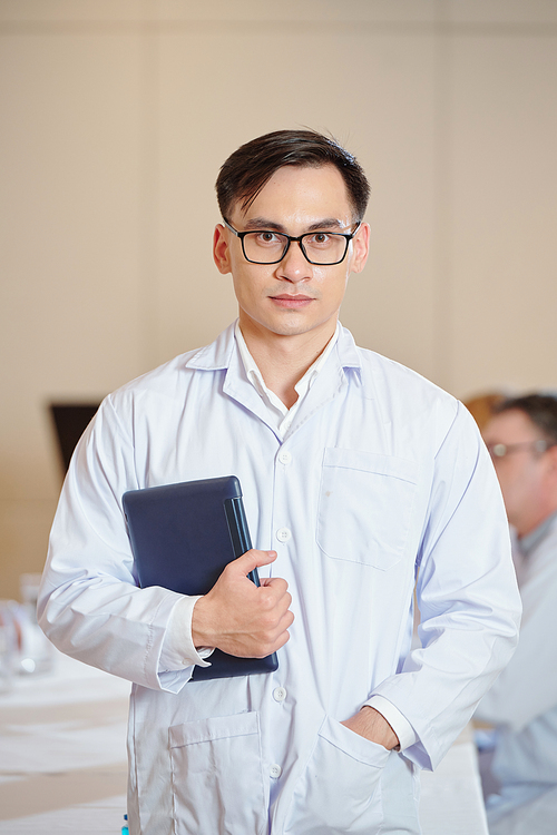 Portrait of young confident researcher in glasses standing in meeting room with digital tablet in hands