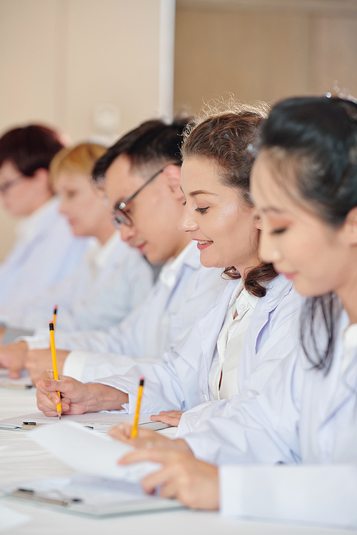 Multi-ethnic group of scientists attending medical conference and talking notes when listening to speaker