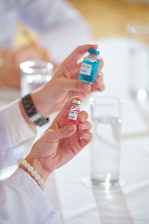 Hands of scientists holding vial with coronavirus vaccines of various colors