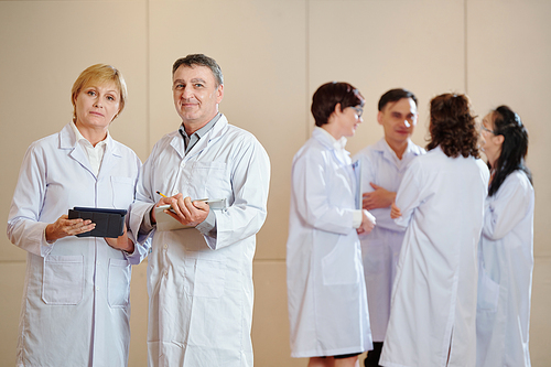 Mature scientists with tablet computers standing in hall after having conference with younger colleagues