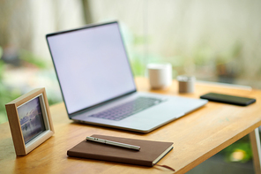 Planner and pen next to laptop on home office desk in room with huge windows