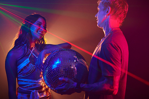 Smiling night club dancer flirting with young man holding disco ball