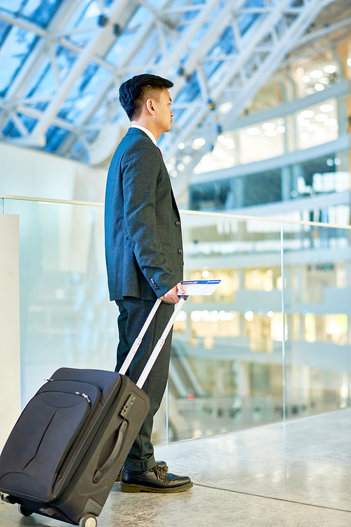 Full length portrait of modern Asian businessman carrying suitcase while crossing airport waiting lounge, copy space