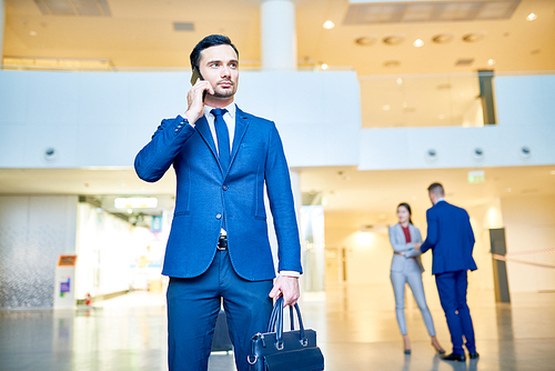Portrait of handsome elegant businesssman speaking by phone holding baggage in modern airport, copy space
