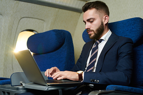 Portrait of handsome bearded businessman using laptop while enjoying flight in first class, copy space