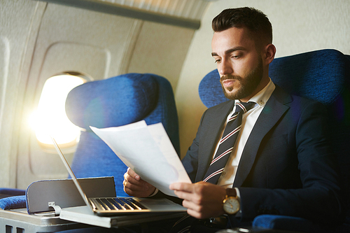 Portrait of handsome bearded businessman working while enjoying flight in first class, copy space