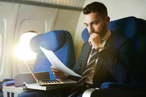 Portrait of handsome bearded businessman reading documents while enjoying flight in first class, copy space