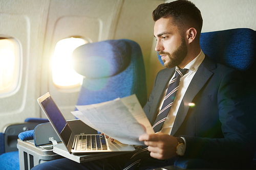 Side view portrait of handsome bearded businessman working while enjoying flight in first class, copy space