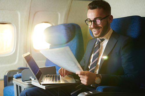 Portrait  of smiling bearded businessman working while enjoying flight in first class, copy space