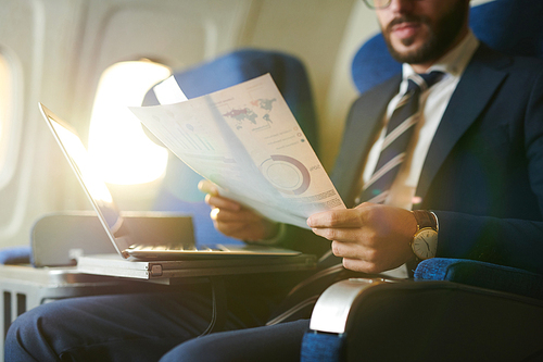 Crop portrait of modern bearded businessman reading documents and working while enjoying flight in first class, copy space